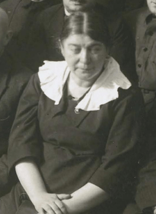 A group photo cropped to show just Esther Frumkin, wearing a plain black dress with an attached white collar