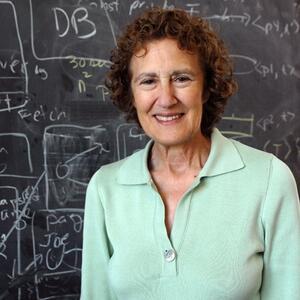 Headshot of Barbara Liskov smiling into camera in front of chalkboard with work