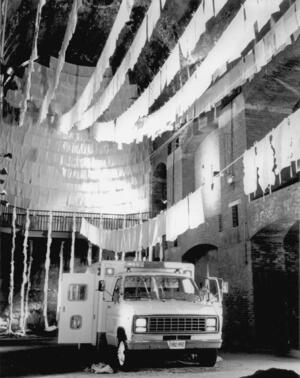 An ambulance parked beneath eight clotheslines hung with pillowcases, with more pillowcases decorating a warehouse space