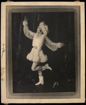 Jean Caroll performing, wearing white boots and an elaborate white costume with fur trim and a feather headdress