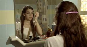 Woman with long dark hair, seen from behind applying eyeshadow in a mirror in Keren Yedaya’s film Jaffa
