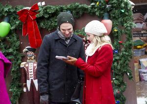A man and woman stand in the snow looking at a notepad