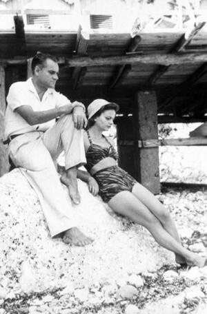 Elsa Morante and Alberto Moravia, sitting on a rock in beachwear. 