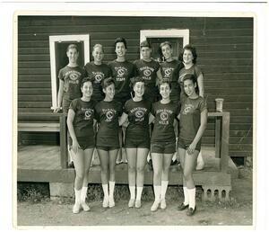 11 girls posed in two rows and smiling outside their bunkhouse