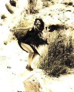 Hester Martinez in a rocky area covered with scrub, posing with her hat in her hand