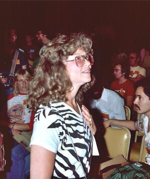Trina Robbins standing in an auditorium, with a large crowd in the seats behind her