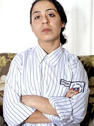 Portrait of a woman with folded arms, wearing a white collared shirt with blue pinstripes and patches