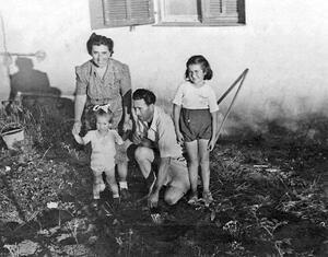 A woman leaning down and holding the hands of a toddler, with a man kneeling beside them and an older girl (Yona Wallach) standing nearby