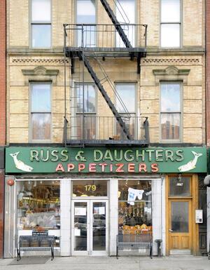 Russ and Daughters storefront in lower Manhattan on first floor of a building with red and green neon lit sign and benches in front of windows
