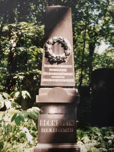 A brown obelisk-style grave with a stone wreath