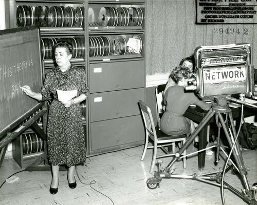 Ida Rhodes (left) working on a chalkboard as a camera films