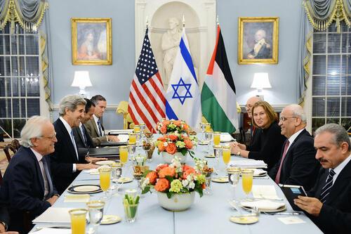 Tzipi Livni seated at formal dinner table with seven other guests, all men, including former U.S. Secretary of State John Kerry and Palestinian chief negotiator Saeb Erekat. The American, Israeli, and Palestinian flags are displayed in the center, at the end of the table.