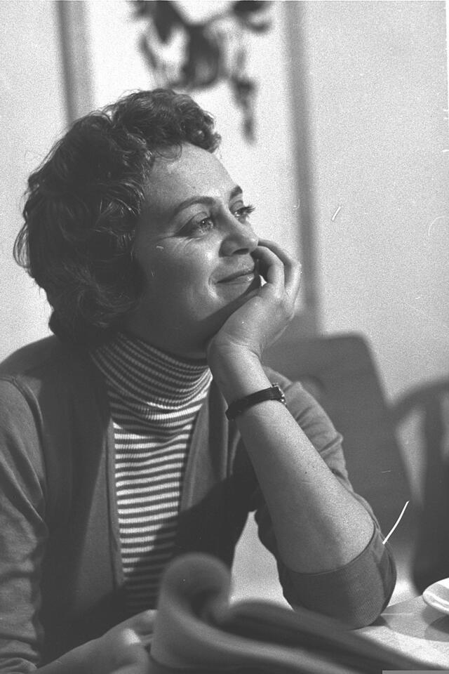 Hanna Maron sitting at a table, smiling with her chin in her hand