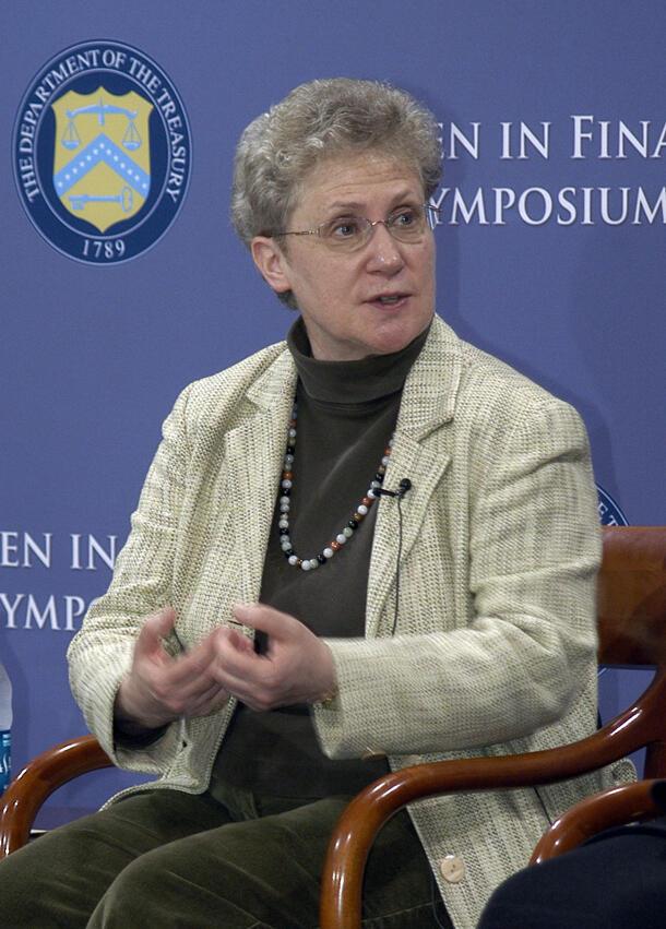 Abby Joseph Cohen speaking while seated in a chair in front of a symposium backdrop