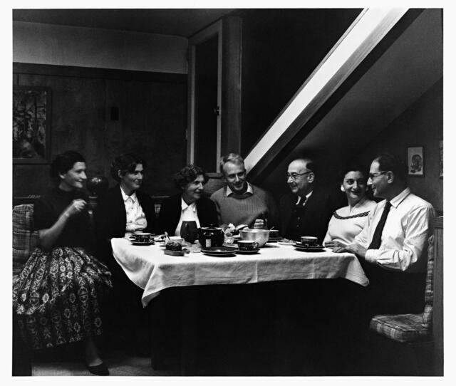 A group of four women and three men sitting at a table with a teapot and cups