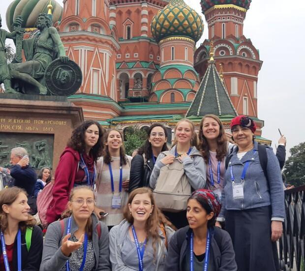 A group of high school girls and a chaperone pose in front of St. Basil's Cathedral