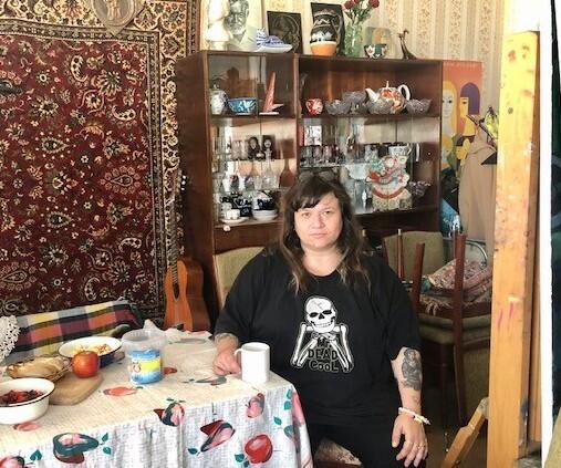 Zoya Cherkassky sitting at a table in a room with china shelves and a Persian rug wall hanging