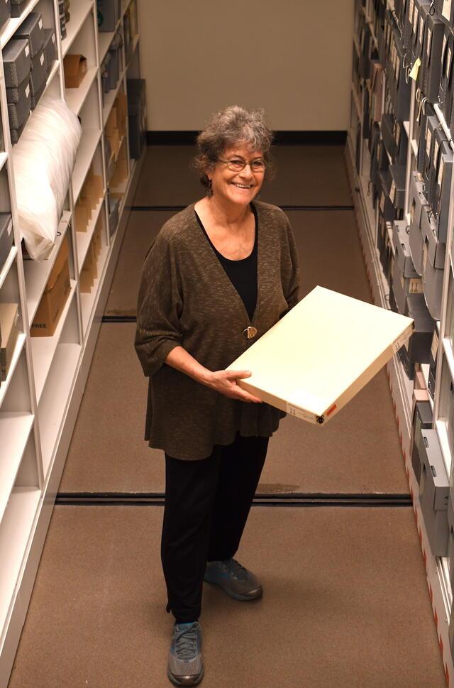 Woman standing holding large box, library shelves in background
