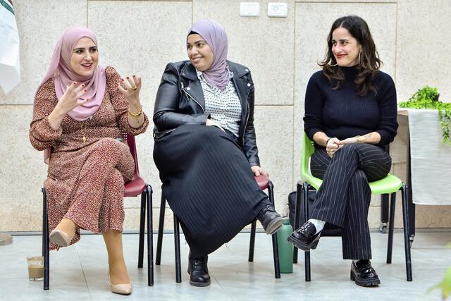 Photo of three women sitting side by side; the woman on the left and in the center have their heads covered, the woman on the right is dressed in black